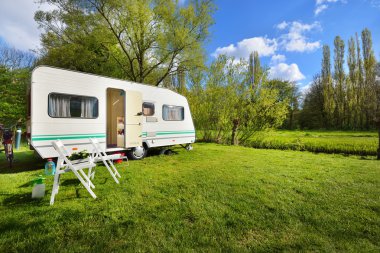 Kamp alanındaki yeşil çimlerde beyaz karavan karavanı. Güneşli bir gün. Bahar manzarası. Avrupa. Yaşam tarzı, seyahat, eko-turizm, yol gezisi, yolculuk, tatiller, eğlence, ulaşım, karavan, karavan