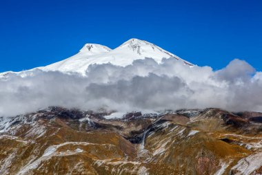 Karlı zirvesi olan dağ manzarası, alçak bulutlar ve mavi gökyüzü, Dombay, Rusya 