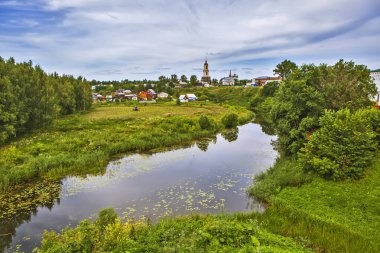 Nehir, evler ve kiliselerle yemyeşil bir manzara.