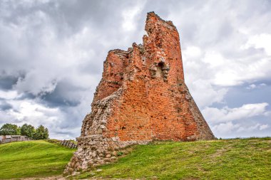 Bulutlu gökyüzünün altındaki yeşil tepede kırmızı tuğla kalıntıları