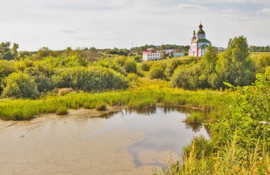 Nehir, evler ve kiliseyle yemyeşil bir manzara.