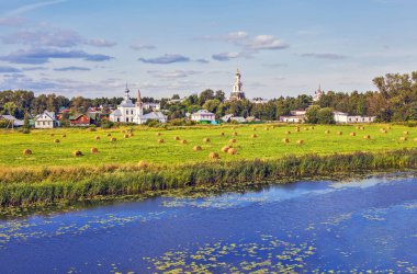 Nehir, evler ve kiliselerle yemyeşil bir manzara.