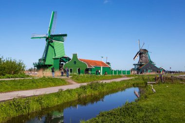 ZAANES-SCHANS, NETHERLANDS - 3 Mayıs 2018: İnsanlar rüzgâr tarlasıyla pitoresk etnoğrafya köyünde yürüyorlar
