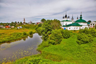 Nehir, evler ve kiliselerle yemyeşil bir manzara.