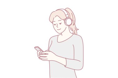 Kulaklık takan genç bir kadın, ses içeriğinden, rahat duruşundan ve gelişigüzel konuşmaktan zevk alırken akıllı telefon kullanıyor.