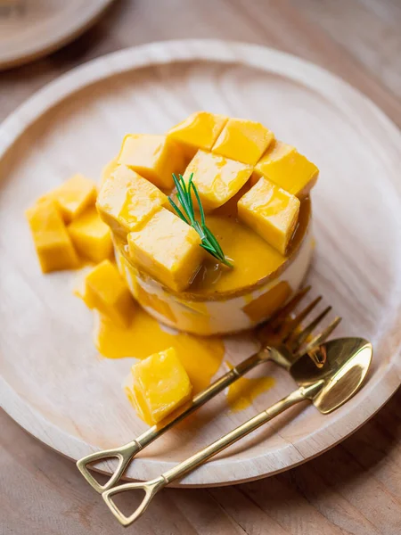 Sweet Yellow Mango dessert, cheesecake. Ripe yellow mango cheesecake serves on the round wooden tray with a small brass spoon and fork. Homemade sweets.