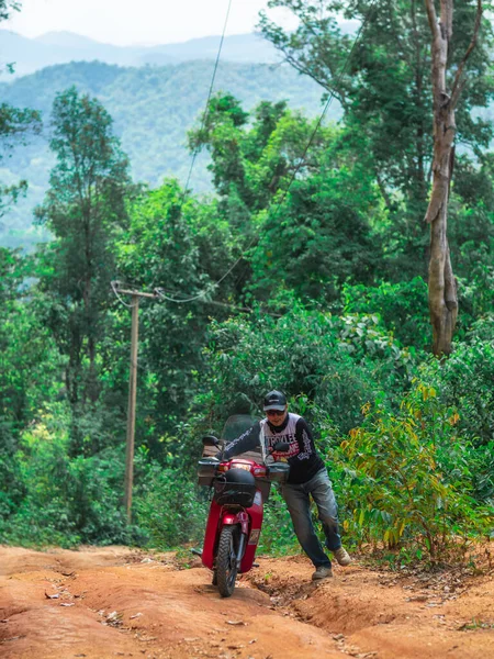 Chiang Mai, Tayland - 22 Mayıs 2021: Arka planda orman ve dağlarla dolu kırsal bir alanda motosikletini yokuş yukarı süren bir adam.