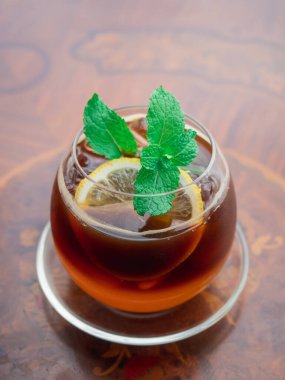Nane yaprağı ve bir dilim limonla süslenmiş buzlu limon çayı. Tahta masadaki top şeklinde bardakta ev yapımı organik buzlu limon çayı. Soğuk içecekler 45 derece, yüksek melek..