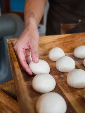 Fırıncı elleri çörekler için hamur hazırlıyor. Tepside bir yığın hamur var..
