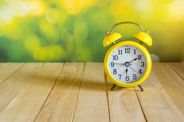 Yellow clock on wood table — Stock Photo, Image