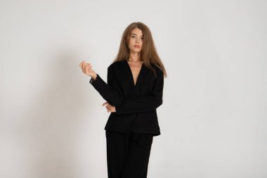 Beyaz arka planda siyah ceketli ve pantolonlu bir kız.