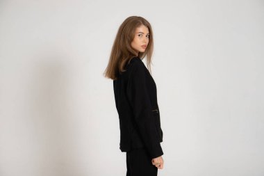 Beyaz arka planda siyah ceketli ve pantolonlu bir kız.