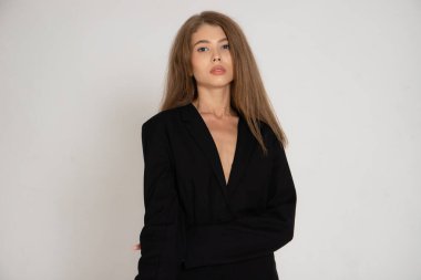 Beyaz arka planda siyah ceketli ve pantolonlu bir kız.