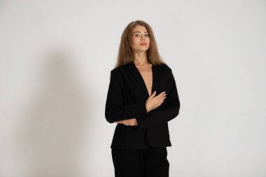 Beyaz arka planda siyah ceketli ve pantolonlu bir kız.