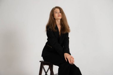 Beyaz arka planda siyah ceketli ve pantolonlu bir kız.