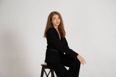 Beyaz arka planda siyah ceketli ve pantolonlu bir kız.