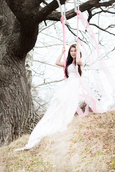 Beautiful woman in white wedding dress shaking on a swing — Stock Photo, Image