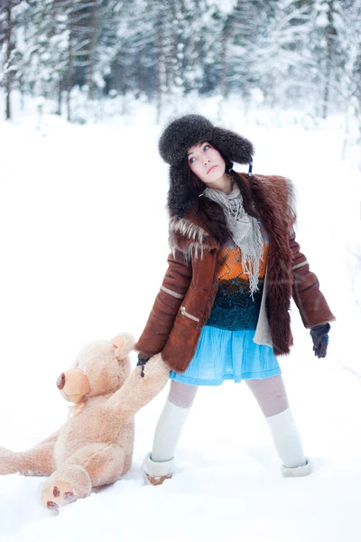 Schöne Mädchen im Winter schneebedeckten Wald Hintergrund mit Teddybär — Stockfoto