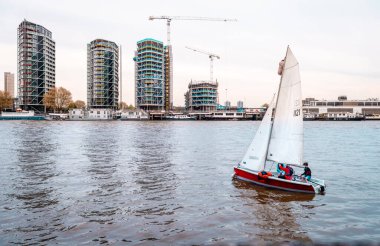 London, UK - April 17 2014: A sailboat on the river Thames. Nine Elms is in the background with residential developments along the riverside.  clipart