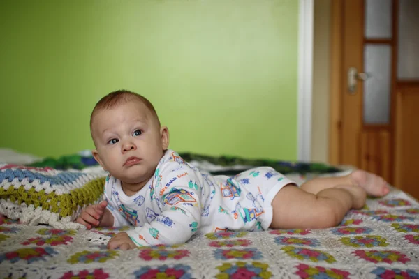 Pequeño niño acostado sobre su estómago y mira . — Foto de Stock