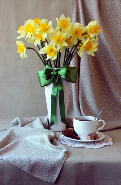 Un vaso con un mazzo di narcisi e una tazza di tè . — Foto Stock