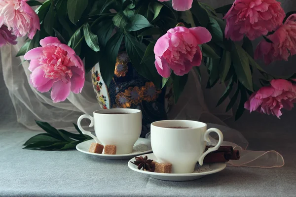 Weiße Tasse Tee auf dem Hintergrund einer Vase mit Pfingstrosen. — Stockfoto