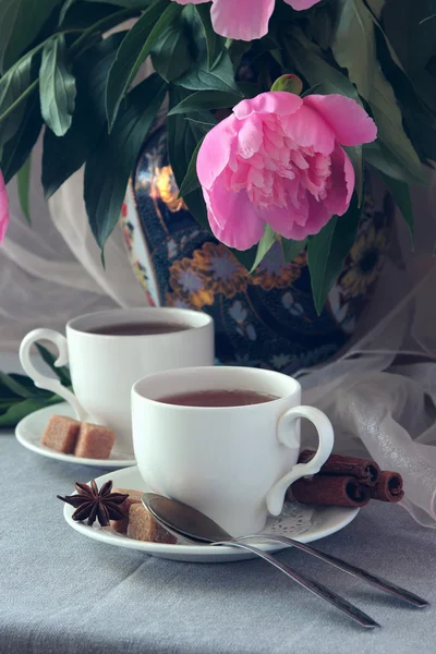 Λευκό φλιτζάνι τσάι με φόντο ένα βάζο με παιώνιες. — Φωτογραφία Αρχείου