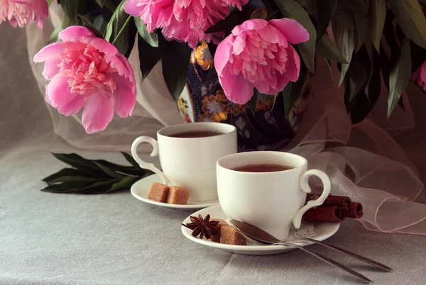 Weiße Tasse Tee auf dem Hintergrund einer Vase mit Pfingstrosen. — Stockfoto