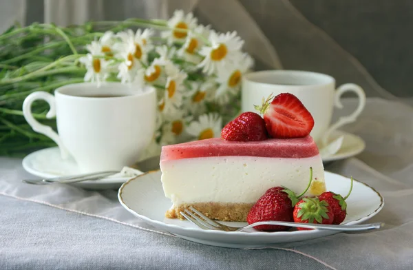 Bir parça kek, beyaz fincan çay ve demet papatya.