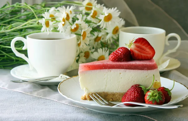 Bir parça kek, beyaz fincan çay ve demet papatya.