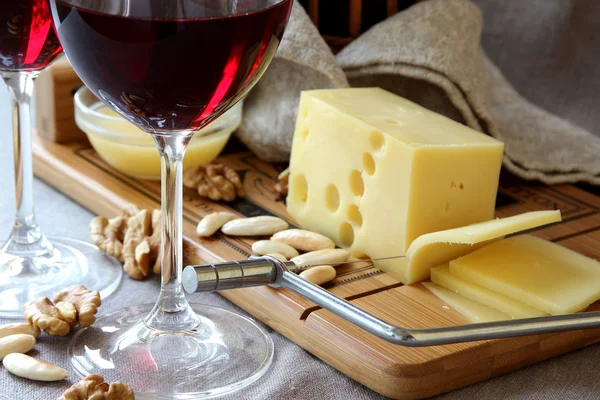 Stukje kaas op een bord, wijn glazen en noten. — Stockfoto