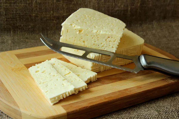 Home cheese, cut into pieces on the board and knife — Stock Photo, Image