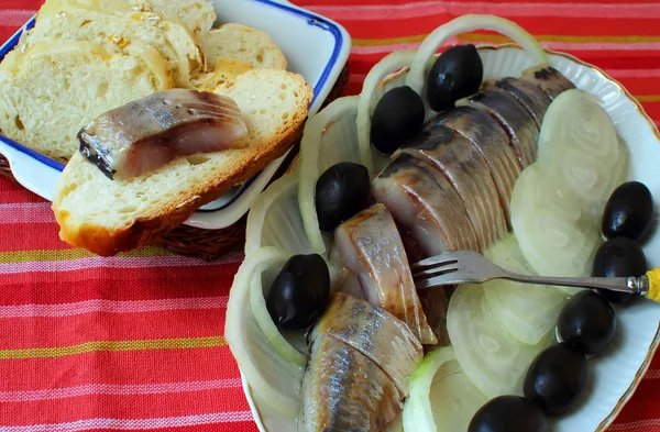 Тарелка сельди, украшенная оливковыми и луковыми кольцами и хлебом — стоковое фото