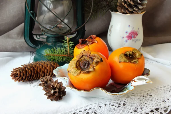 Weihnachtsstillleben mit Kaki und Tannenzapfen — Stockfoto