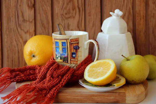 Tasse de thé chauffante, attachée avec une écharpe et des fruits — Photo