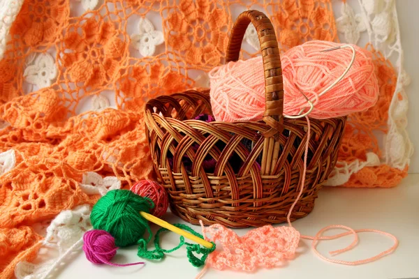 Several balls of colored yarn and a hook for tying lying near basket — Stock Photo, Image