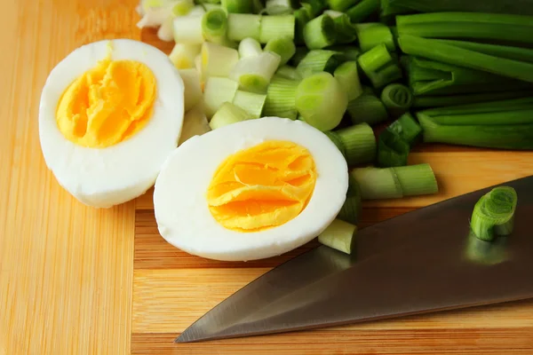 Egg, cut in half, and green onion on the board — Stock Photo, Image