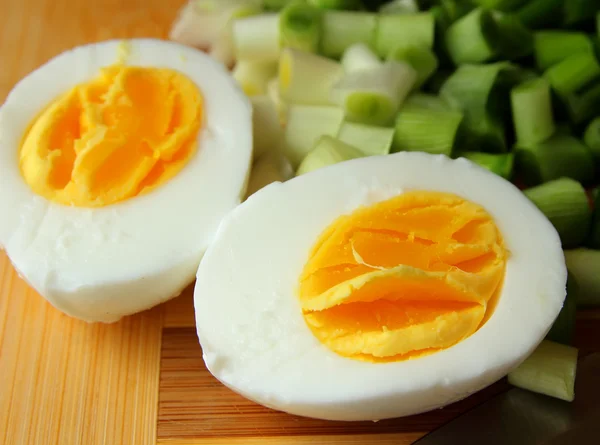 Egg, cut in half, and green onion on the board — Stock Photo, Image