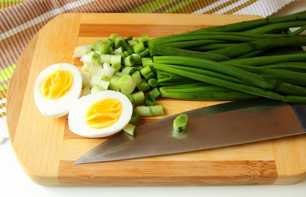 Egg, cut in half, and green onion on the board — Stock Photo, Image