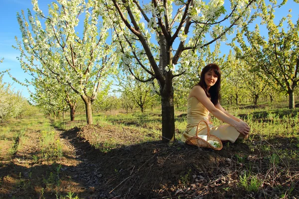 Schöne Mädchen sitzt unter einem Baum auf einem Hintergrund von blühenden Garten — Stockfoto