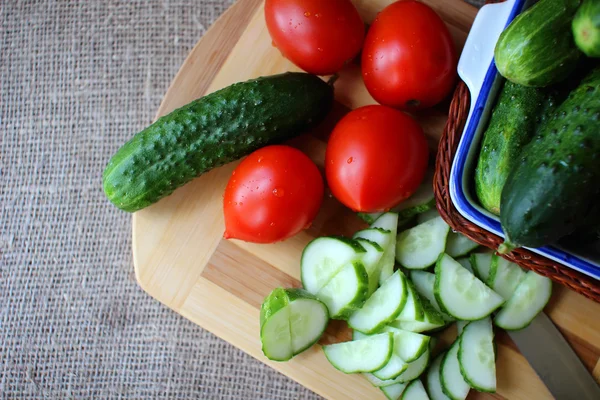 Pepinos y tomates acostados sobre el tablero y ensalada picada — Foto de Stock