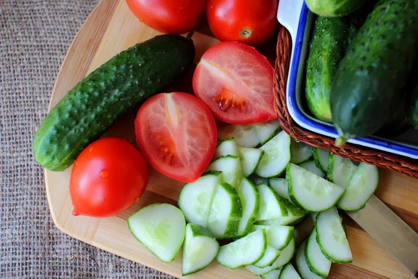 Pepinos y tomates acostados sobre el tablero y ensalada picada — Foto de Stock