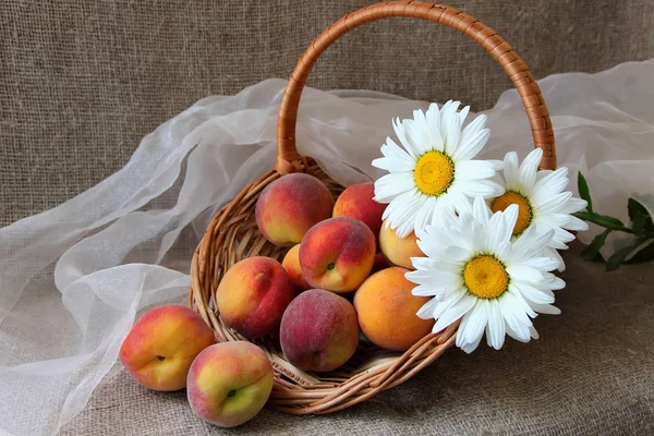 Basket with ripe peaches and bunch of daisies — ストック写真