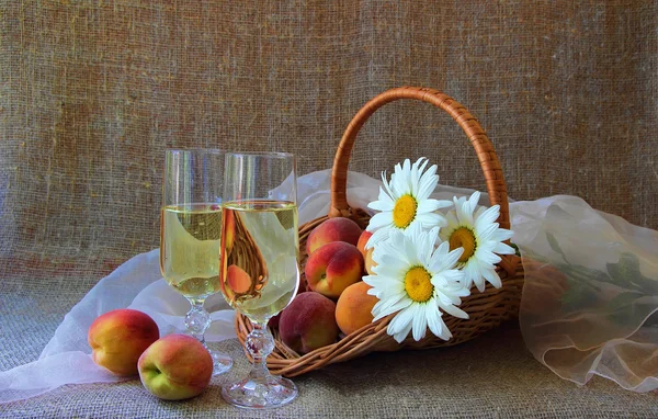 Два бокала белого вина, персики и букет маргариток — стоковое фото