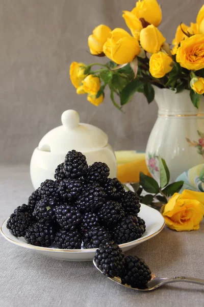 Untertasse mit Brombeeren und einer Vase mit gelben Rosen — Stockfoto