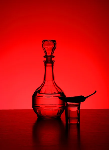 Karaf met wodka en hete peper op een rode achtergrond — Stockfoto