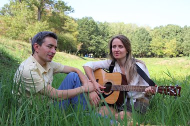 Güzel kız doğa üzerinde bir çocuk için gitar çalmak.