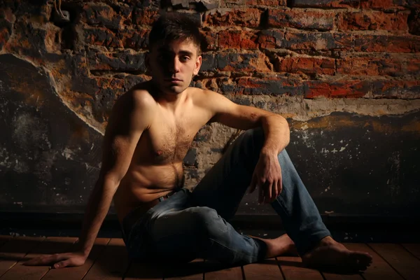 Un joven en jeans sentado con la pared de ladrillo torso desnudo . — Foto de Stock