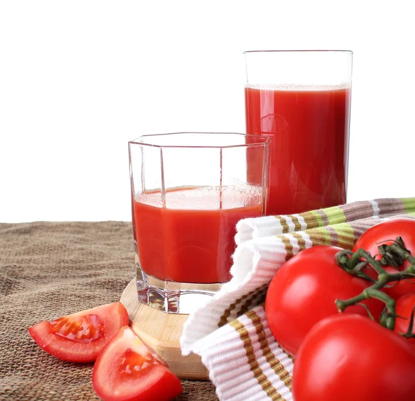 El jugo de tomate se vierte en vasos y tomates maduros sobre un fondo blanco . —  Fotos de Stock