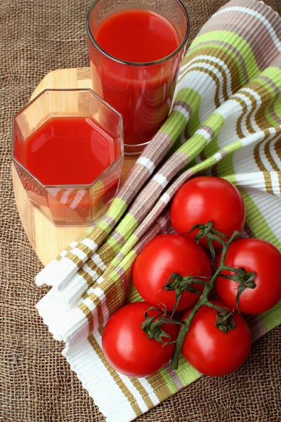 El jugo de tomate se vierte en vasos y tomates maduros . —  Fotos de Stock